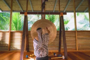 Facilitator playing a gong during a sound healing session at Templo del Tigre retreat center in the Costa Rican jungle near Corcovado National Park.